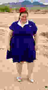 a woman wearing a blue dress, red fascinator standing with mountains in the background