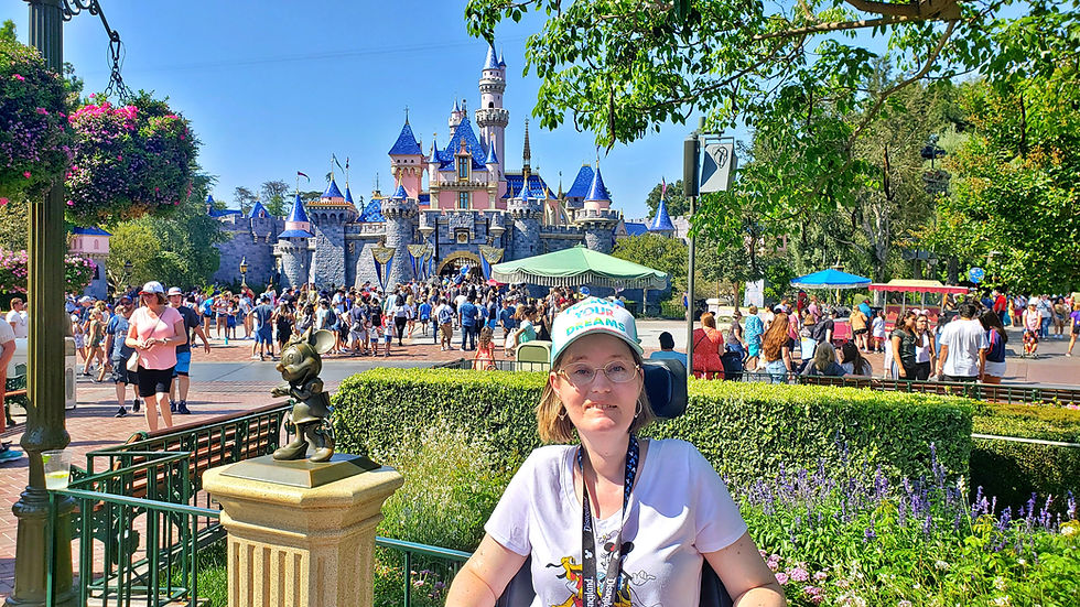 woman in a power wheelchair wearing a hat that says follow your dreams with the Disneyland Castle behind her