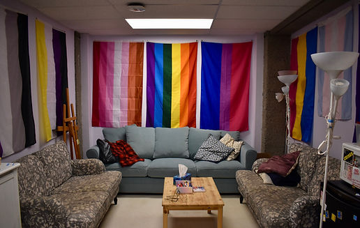 Image of the QM office, showing 3 couches and a small table, on the walls there are pride flags, including asexual, non-binary, gay, lesbian, bisexual, pansexual, and trans