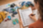 Personne vérifiant une liste de voyage imprimée intitulée "Globe-Trotting". Arrière-plan : valise, effets personnels et vêtements colorés.