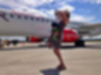 Une maman portant un bébé devant un avion, sur le tarmac.