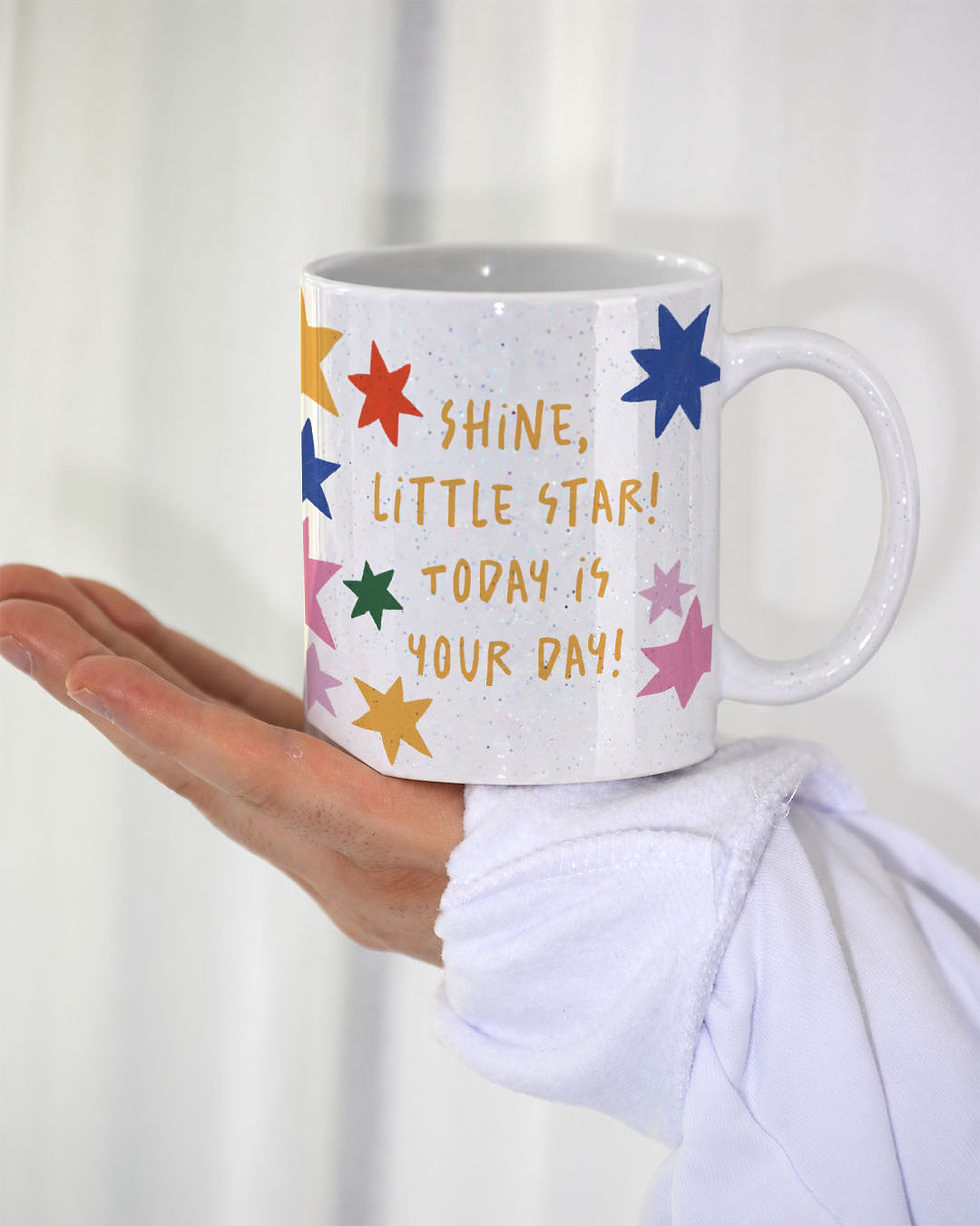 Miniaturbild: Weiße Keramiktasse mit feinen Glitzerpartikeln und einer Zeichnung aus bunten Sternen. Die Tasse trägt den Spruch „SHINE, LIT