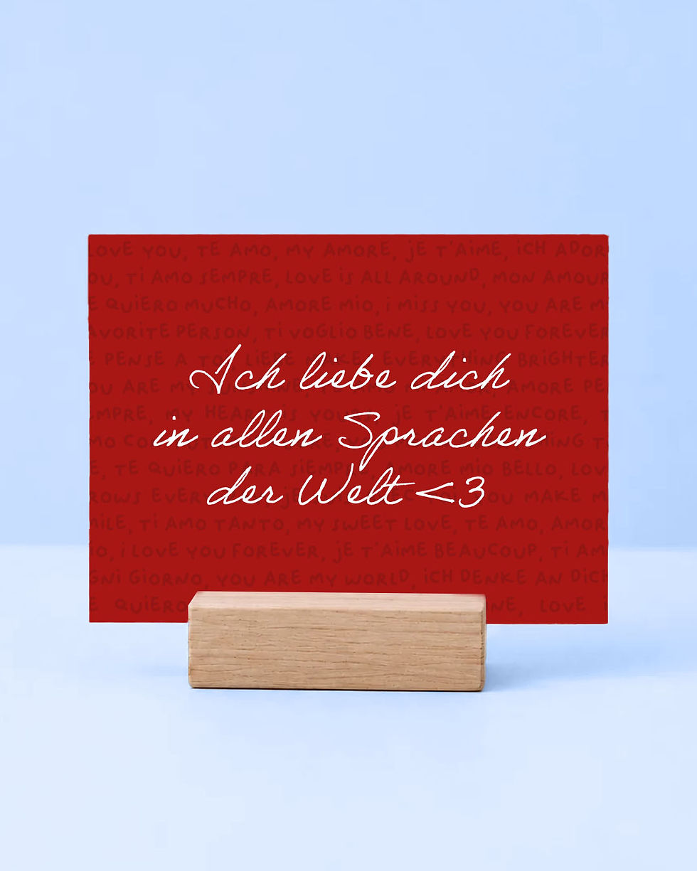 Eine rote romantische Postkarte mit dem weißen handgeschriebenen Spruch „Ich liebe dich in allen Sprachen der Welt“