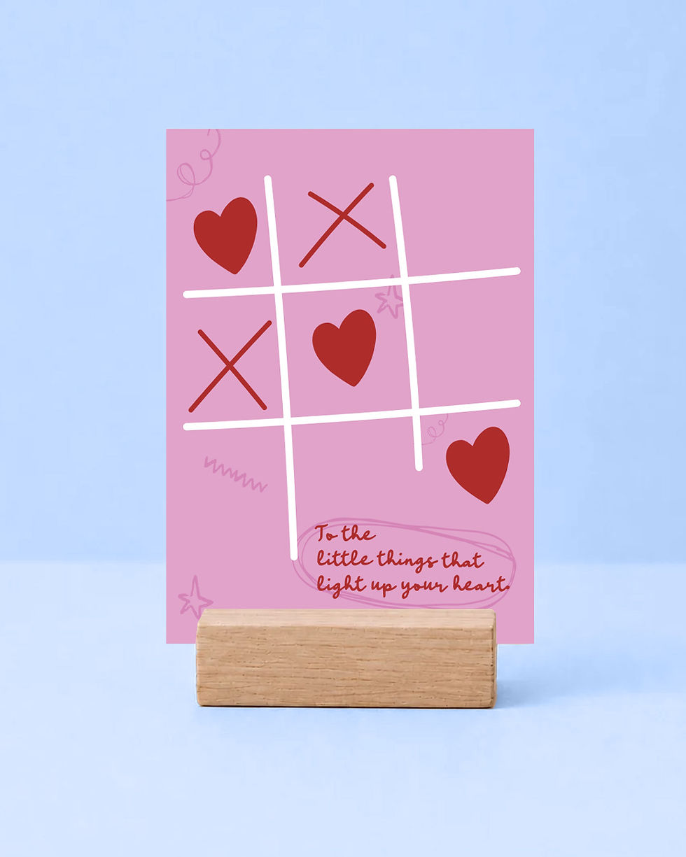 Rosa Grußkarte mit einem Tic-Tac-Toe-Spiel aus roten Herzen und Kreuzen sowie dem handgeschriebenen englischen Spruch „To the