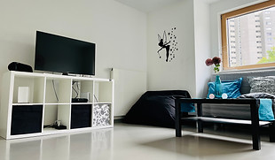 Mädchenzimmer mit weißem TV-Regal und Fernseher, einem Sitzsack, grauem Couch und schwarzem Tisch.