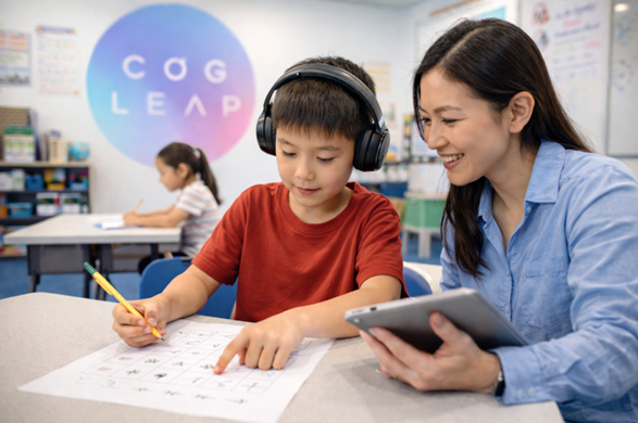Teacher guiding a young boy working on a worksheet in a classroom while he wears headphones, with another child working at a desk in the background and a Cogleap logo on the wall.