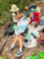 Forest School children working on projects outdoors. One is working on a bow and arrow, one is decorating wind chimes and others are making bird calls.