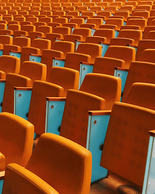 Numerous empty orange seats in an auditorium, arranged in consecutive rows, highlighting the pattern and repetition of seating