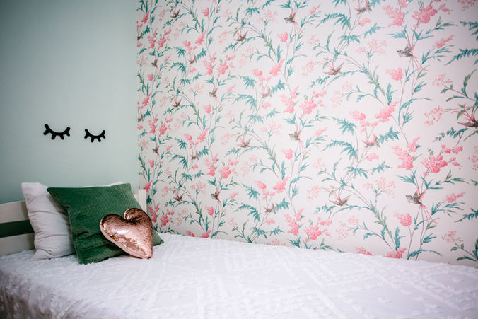 Floral wallpaper and a heart-shaped pillow beside a green pillow.