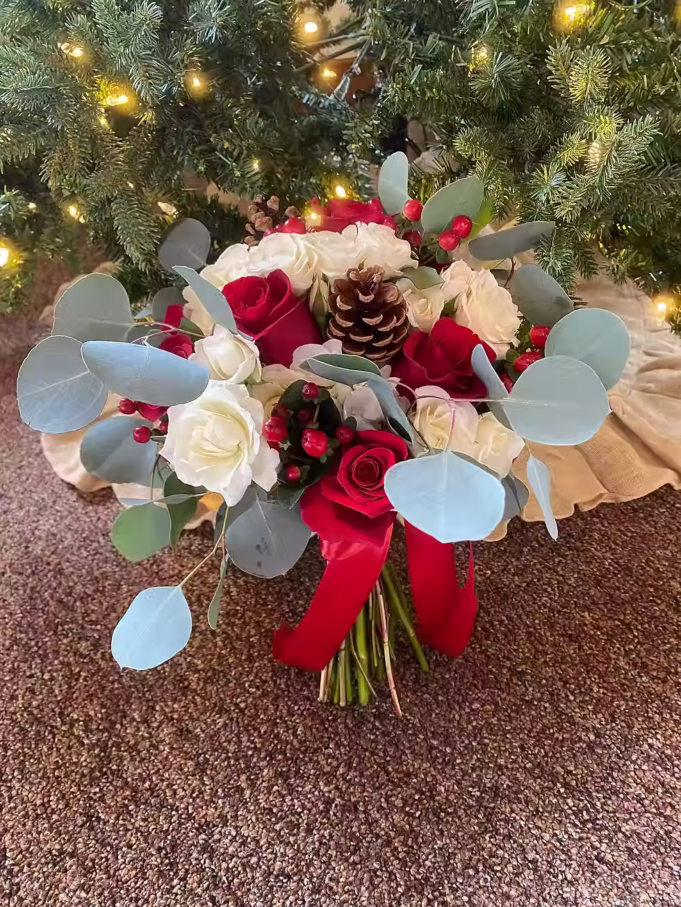 Price: $150.00
The perfect winter themed bouquet with red roses, cream spray roses, red coffee bean, silver dollar eucalyptus, and pinecones