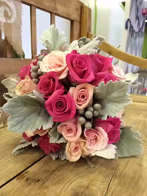 Price: $150.00
This bouquet includes roses in shades of pink, with silver brunia and dusty miller throughout.