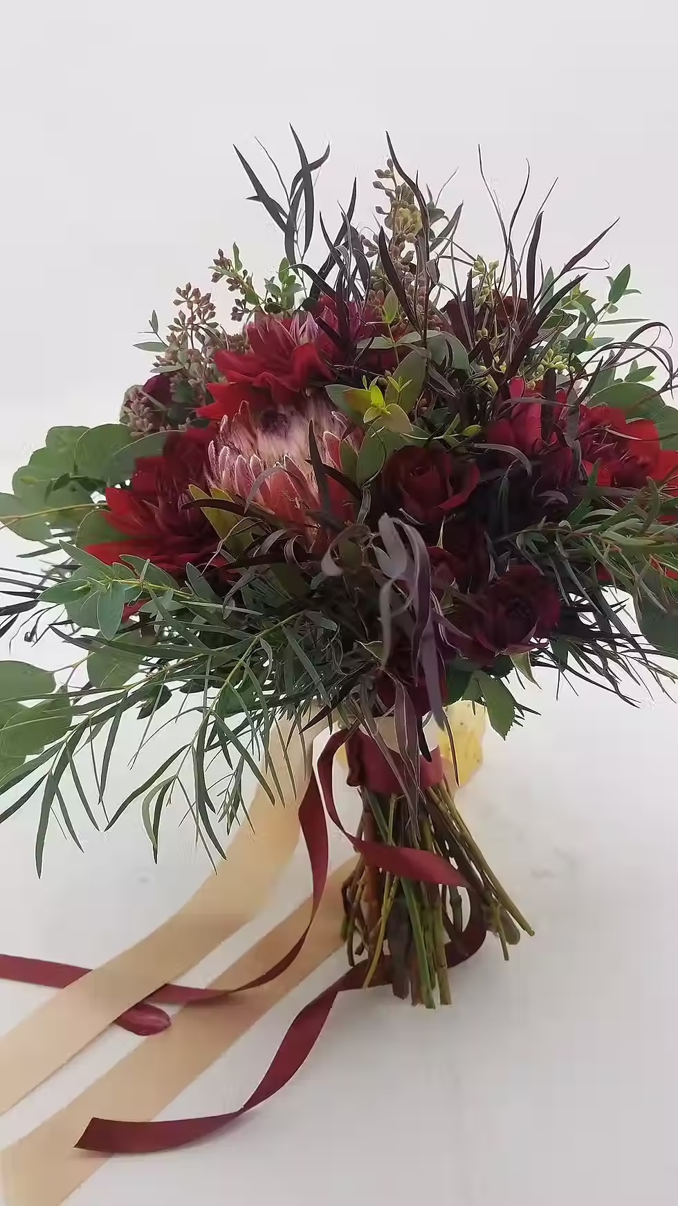 Price: $265.00
A mix of proteas, Rubicon spray roses, and dahlias are accented by agonis, feather eucalyptus, gunni, eucalyptus, and silver dollar eucalyptus.