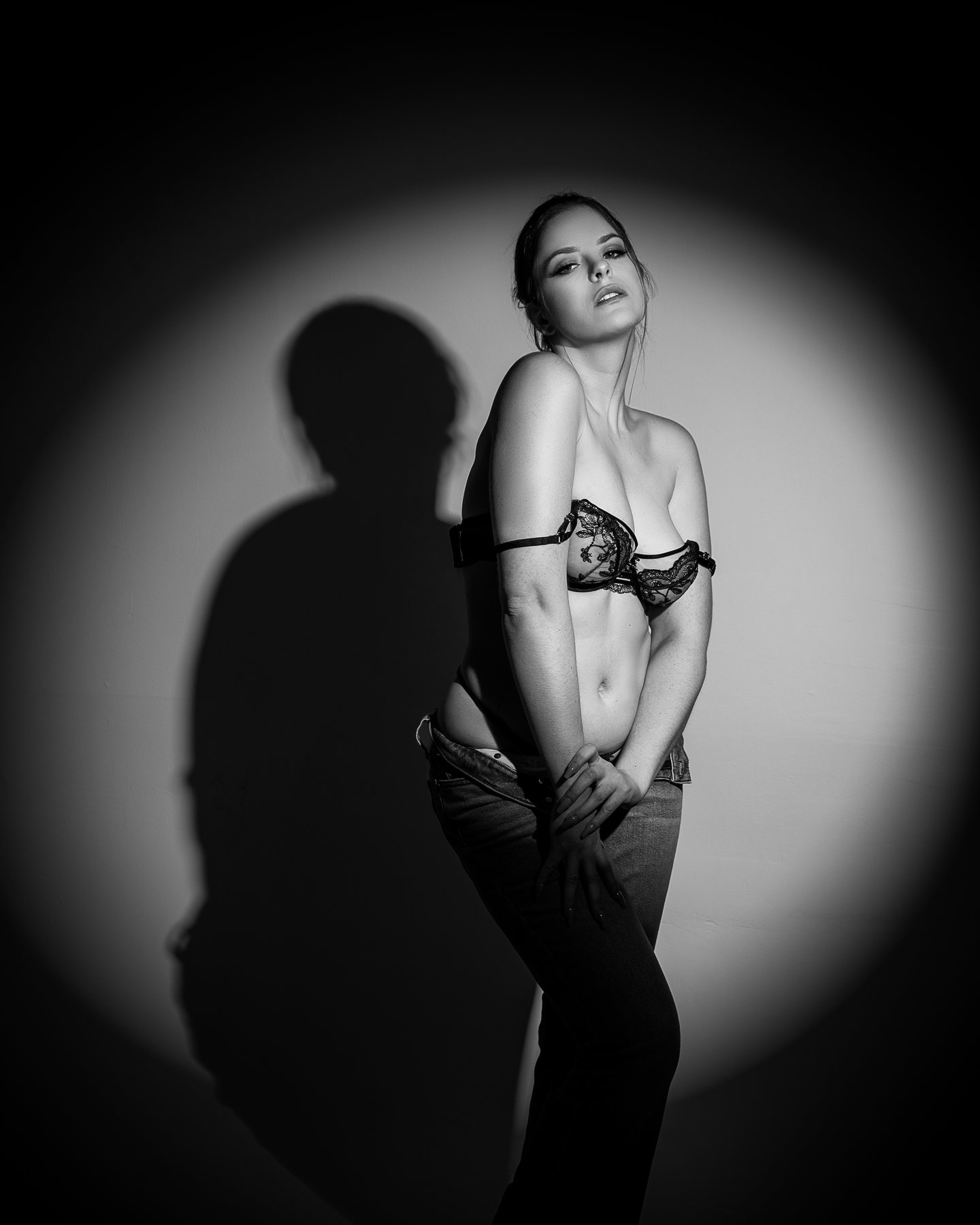 Black and white Austin boudoir portrait of a woman in a lace bra under a round spotlight with her shadow on the wall