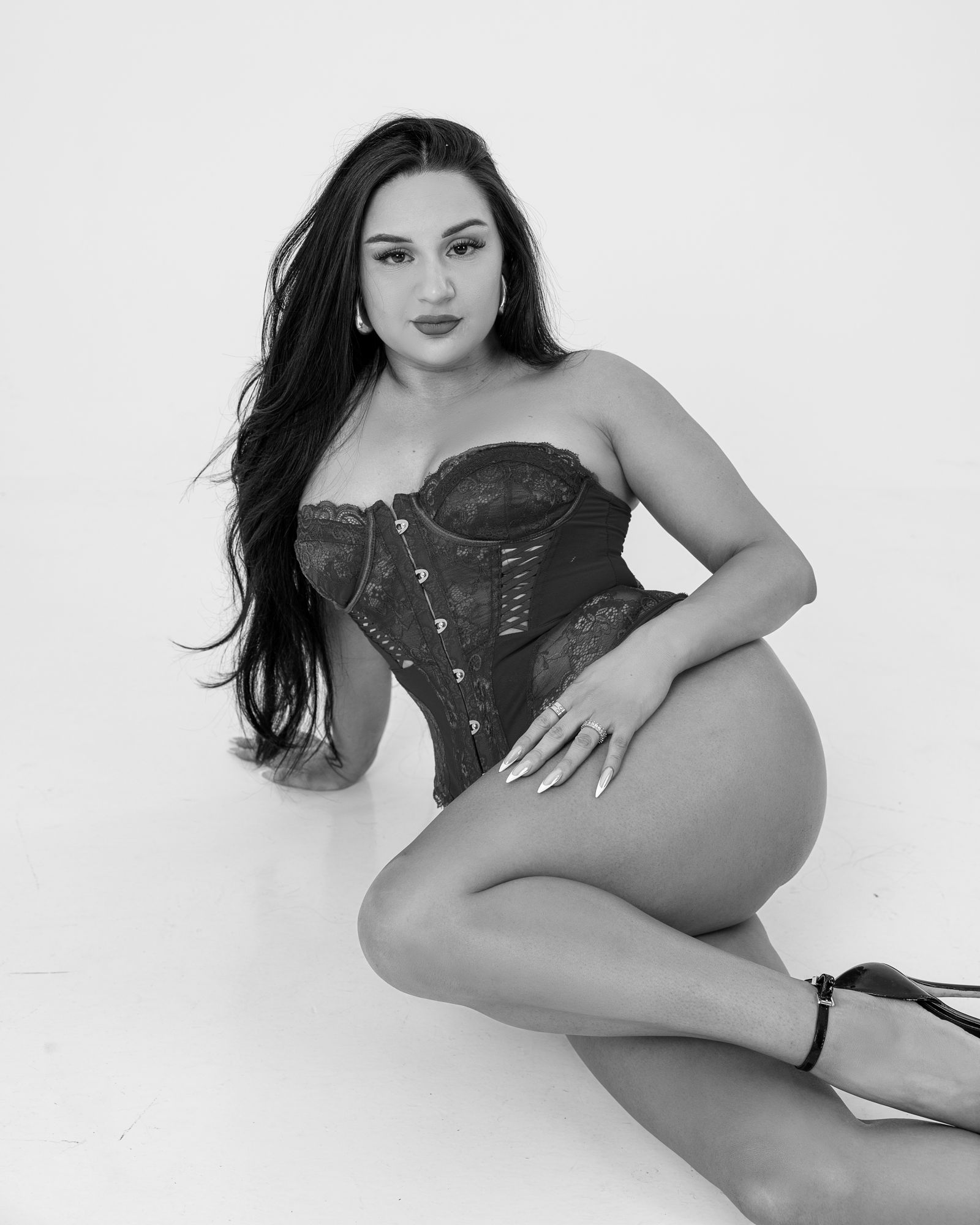 Black and white studio boudoir portrait of a woman in a lace corset seated on the floor