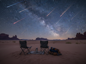 Wide-angle view of a quiet desert campsite under Perseid meteors