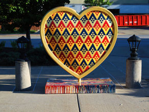 Vibrant geometric heart sculpture on urban pavement, framed by street lamps