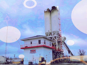 SRM Concrete plant with tall silos and conveyor under a blue sky, industrial yard, white and red building, calm scene