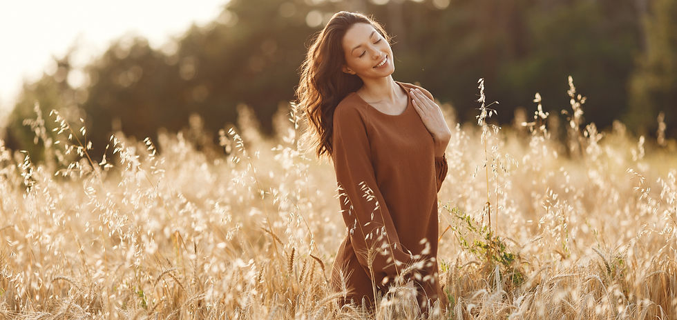 Mujer feliz en un campo de verano al atardecer; transmite calma, libertad y conexión con la naturaleza
