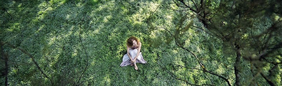 Vista cenital de mujer descalza sentada sobre musgo, rodeada de árboles; grounding en plena naturaleza