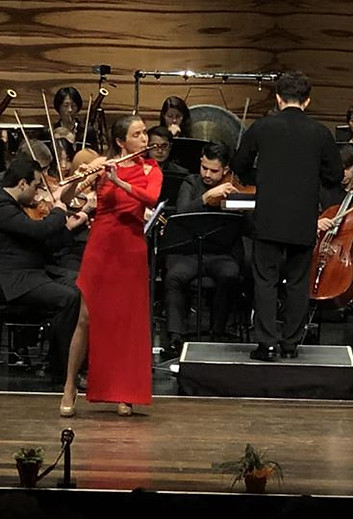 Woman in red dress playing flute with an orchestra