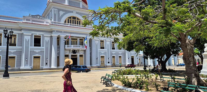 Woman walking past a red-domed building in a sunny town square.