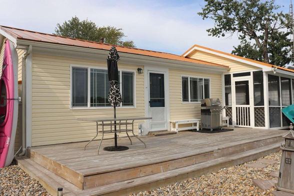 An image of the front of the Fun at the Lake cottage, a yellow cottage with a large deck in front and screened in porch on the right side.