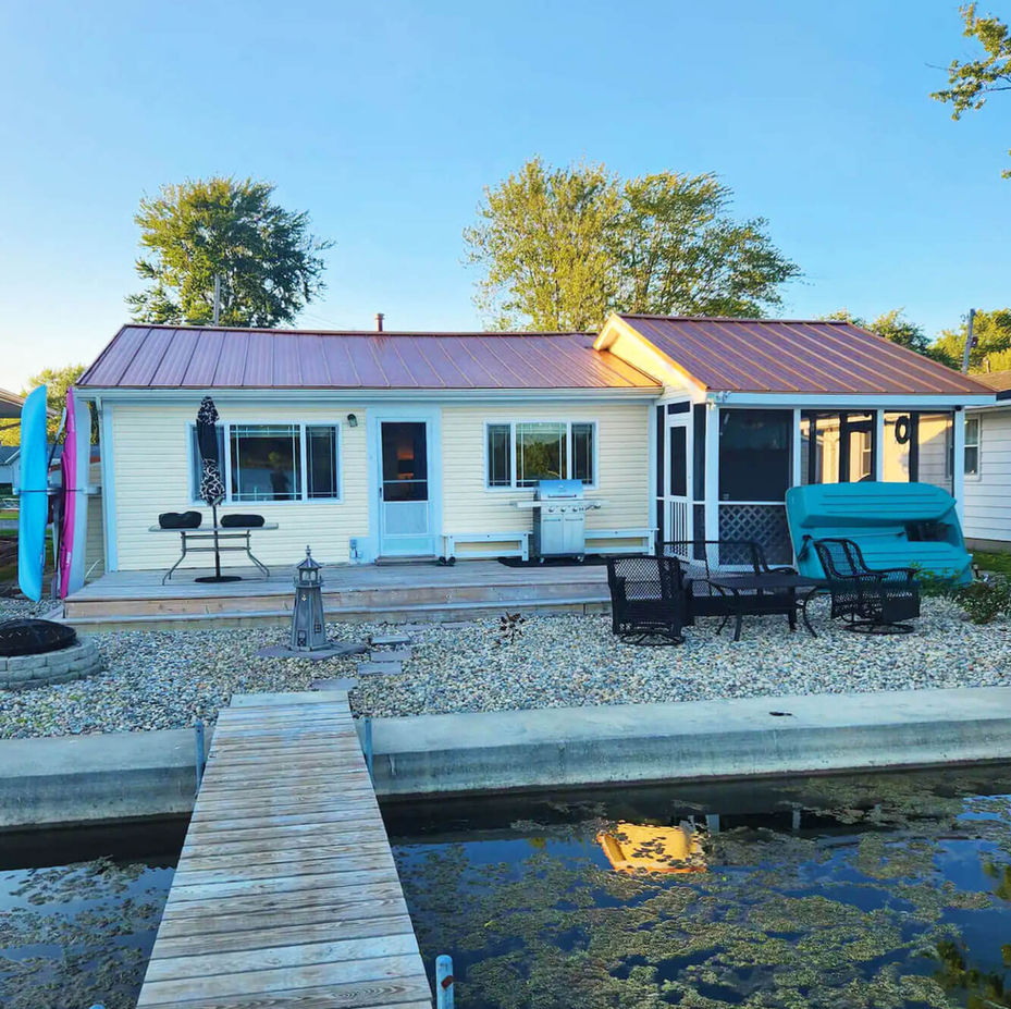 Front view of Fun at the Lake house, a yellow cottage with a large front deck and a dock extending out into the lake.