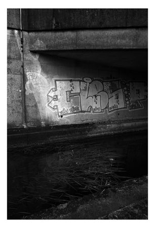 Black and white photograph of the Tennant Canal in South Wales. Bridge and graffiti in strong sunlight and shadows.