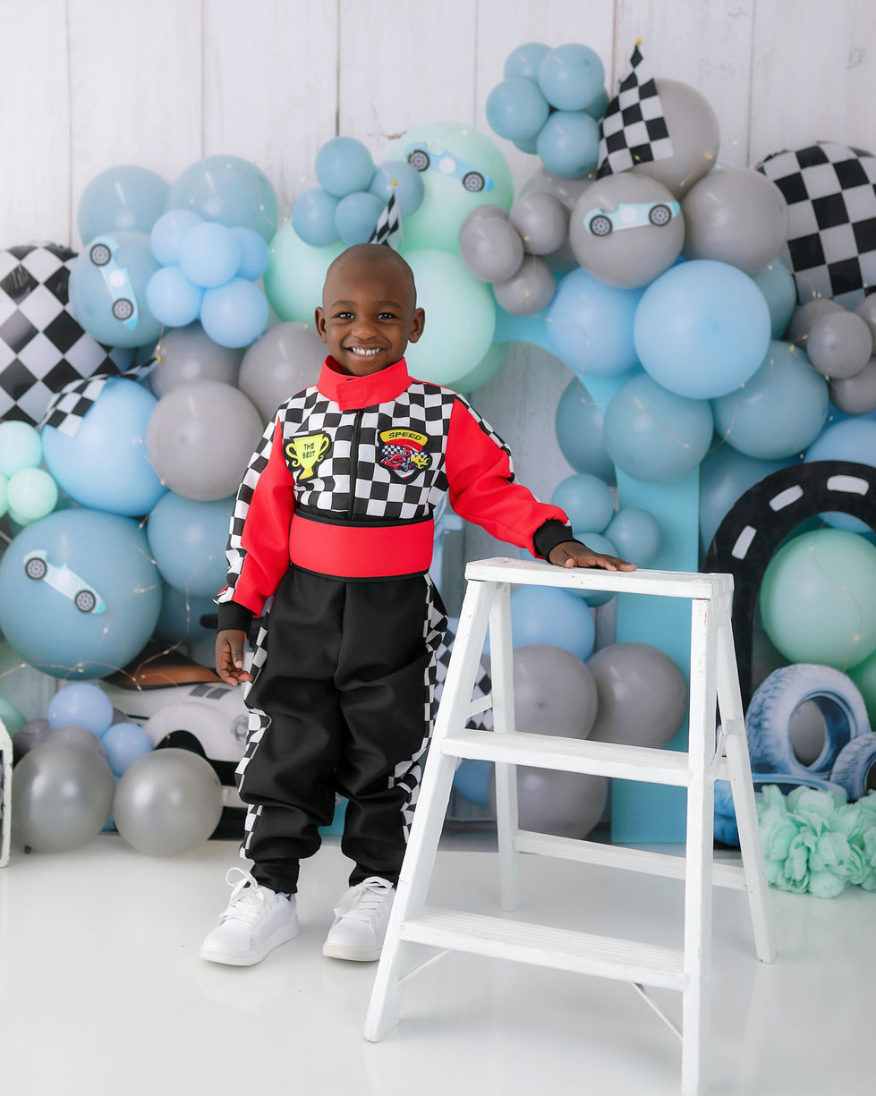 Pastel racing birthday backdrop with blue, grey, and mint balloons, checkered flags, mini cars, tires, and a vintage pedal car – perfect for toddler portraits