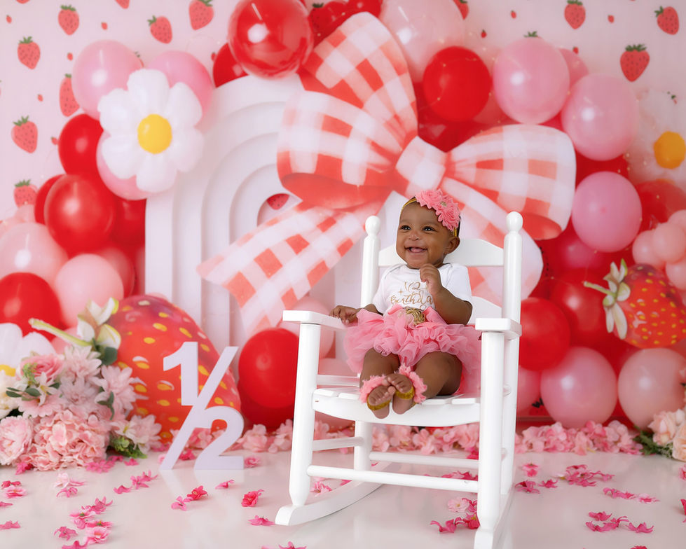 Strawberry-themed birthday backdrop with red and pink balloons, gingham bow, daisies, and strawberry props – ideal for cake smash and first birthday photography