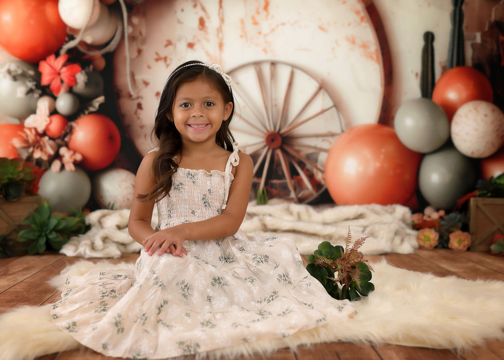 Rustic desert-themed cake smash backdrop with sage and terracotta balloons, wagon wheels, dried flowers, and cacti – perfect for first birthday photography