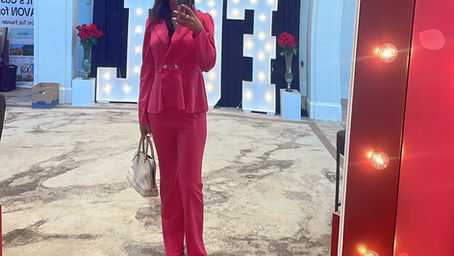 Women in a hot pink suite taking a mirror body selfie, holding a white Purse and has white boots on.