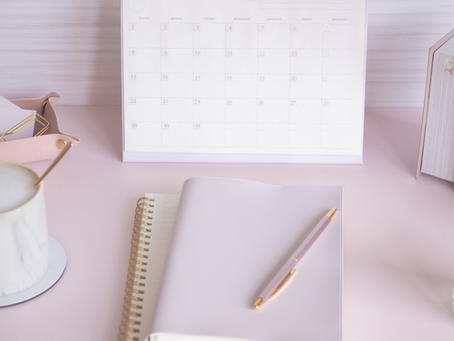 Pink desk with notepad, calendar, coffee mug, candle, and paper clip holder.