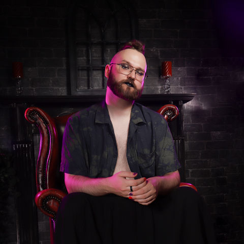 masc non-binary boudoir image of a person posing in a skirt on a red Chesterfield and looking powerful