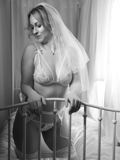 female in bridal lingerie on a white bed, looking dreamily away from the camera