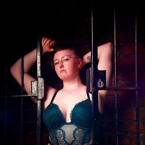 a masc presenting person in lingerie posing with iron gates