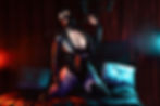 an edgy boudoir image of a latex model wearing a hood, posing on a bed