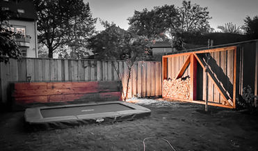 Illuminated raised bed and wooden firewood storage in a garden with a trampoline