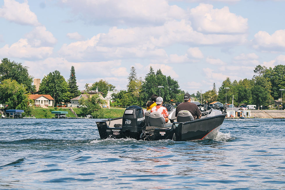 Boat with three people on a lake, lush trees and houses in the background, under a partly cloudy blue sky. Text: "Mercury 115."