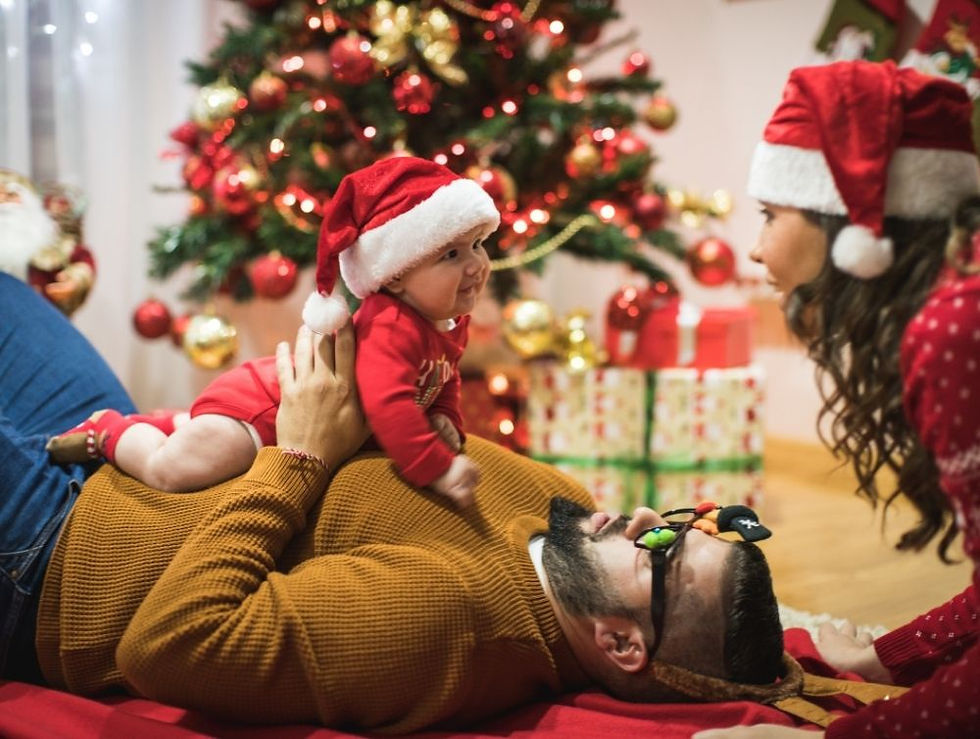 Family in Christmas attire plays near a decorated tree with gifts. Baby in Santa hat smiles at mother, festive and joyful scene.