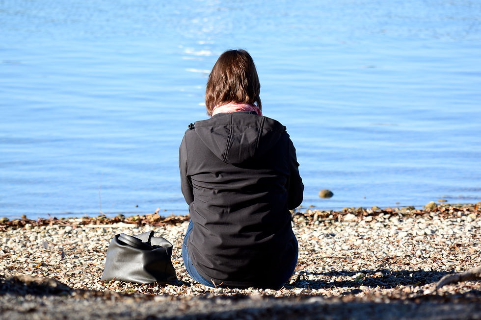 Woman sitting by the water reflecting on people pleasing and emotional exhaustion