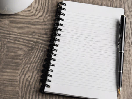 an open notebook with pen lying on a desk