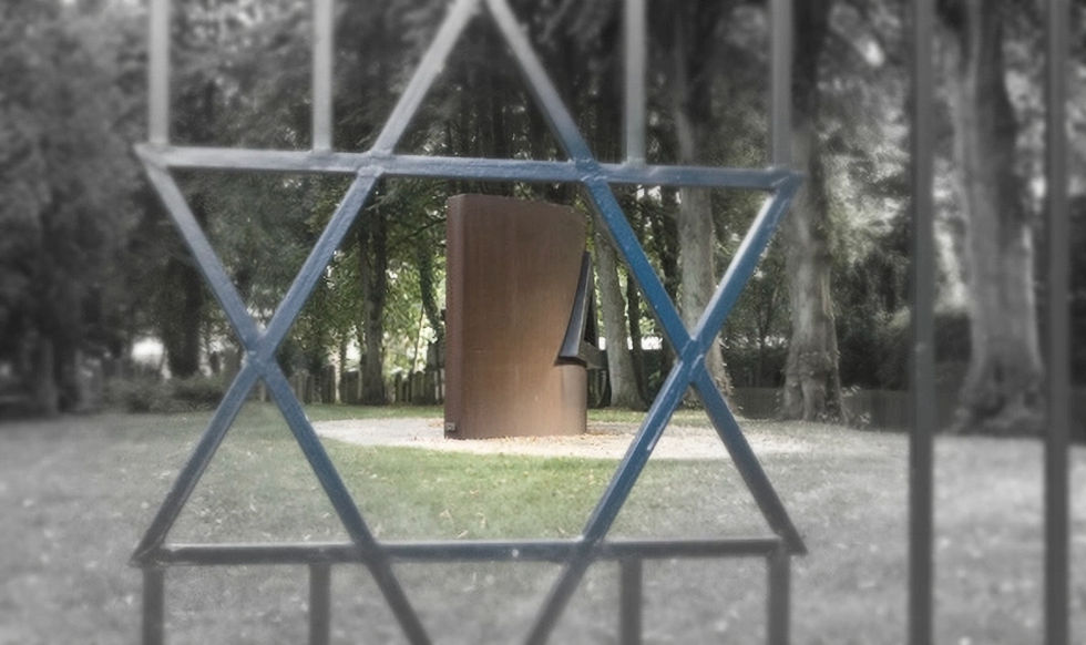 Blick duch einen Zaun auf Denkmal unter Bäumen