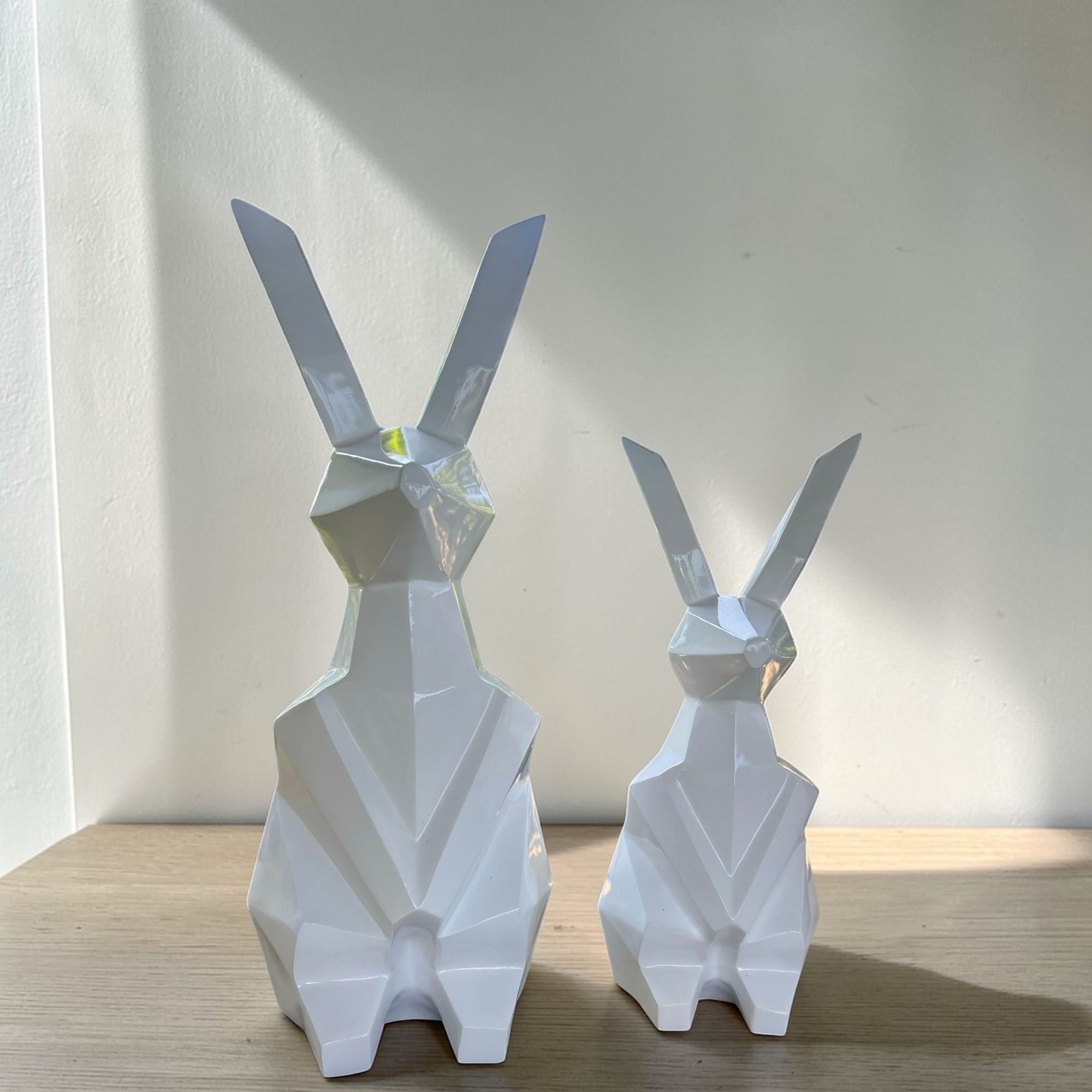 รูปปั้นกระต่ายคู่ดีไซน์โมเดิร์นโพลีกอนสีขาว จัดวางบนฉากหลังสีชมพู ดูเรียบหรูและทันสมัย