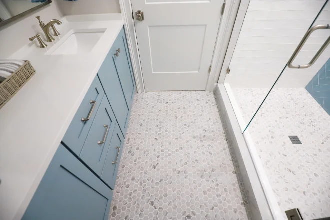 A view of a bathroom featuring a hexagon tile floor, light blue vanity, and a glass shower enclosure.