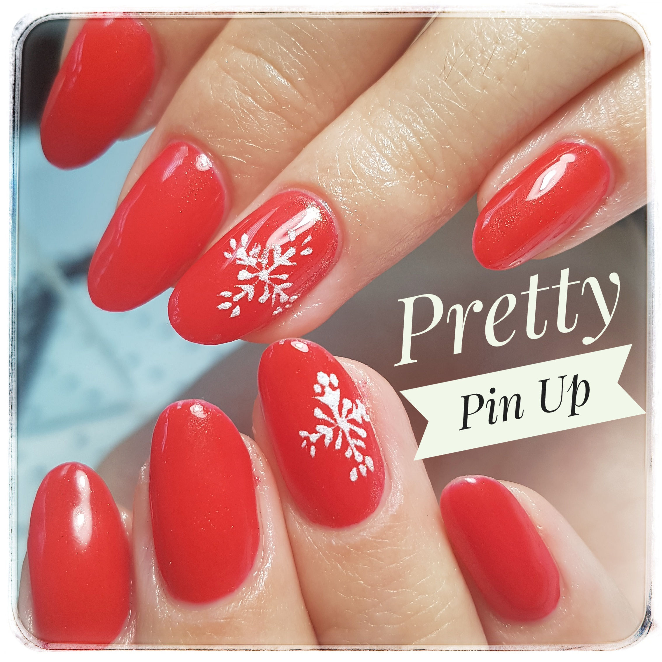 Gros plan sur des ongles longs, colorés en rouge avec un décor de flocon blanc sur les 2 annulaires