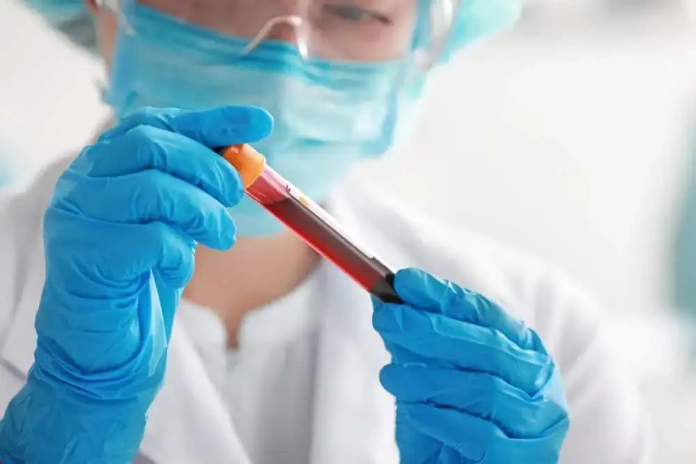 Technician wearing blue gloves examining blood sample tube during lab setup in Rancho Santa Fe, California – USALCS laboratory validation and QC services.