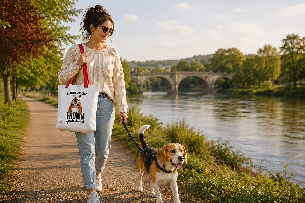 Smiling woman walks a beagle along a riverside path by a stone bridge, carrying a tote that reads TURN YOUR FROWN upside down!