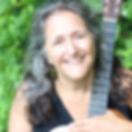 A white woman with long gray-brown hair holds a guitar.