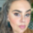 A white woman with long, wavy brown hair and a beige shirt.